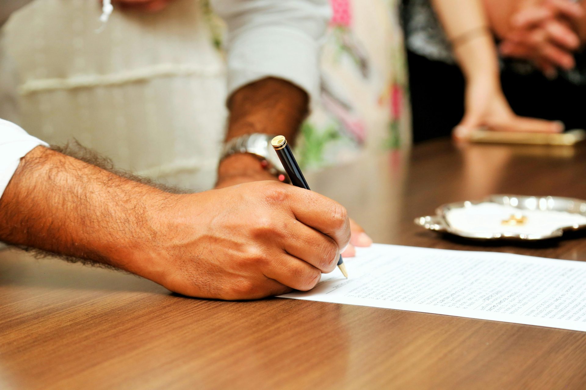 Close-up view of a person signing an important document with a pen on a wooden table.